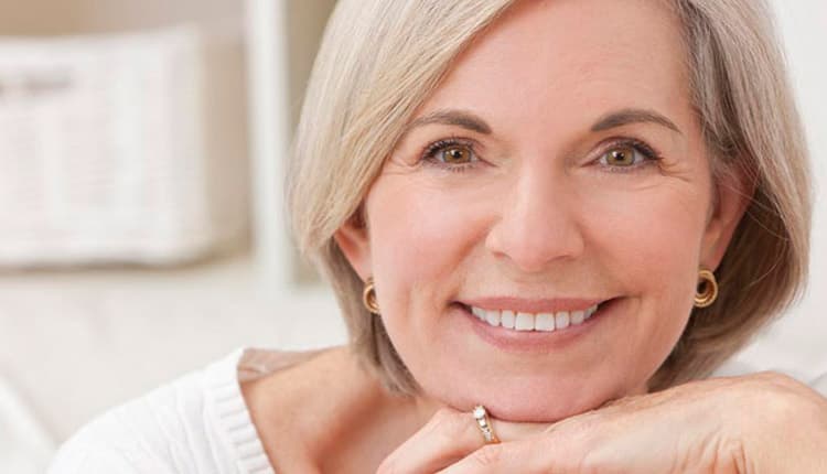 Smiling middle-aged woman with short blonde hair resting her chin on her folded hand.