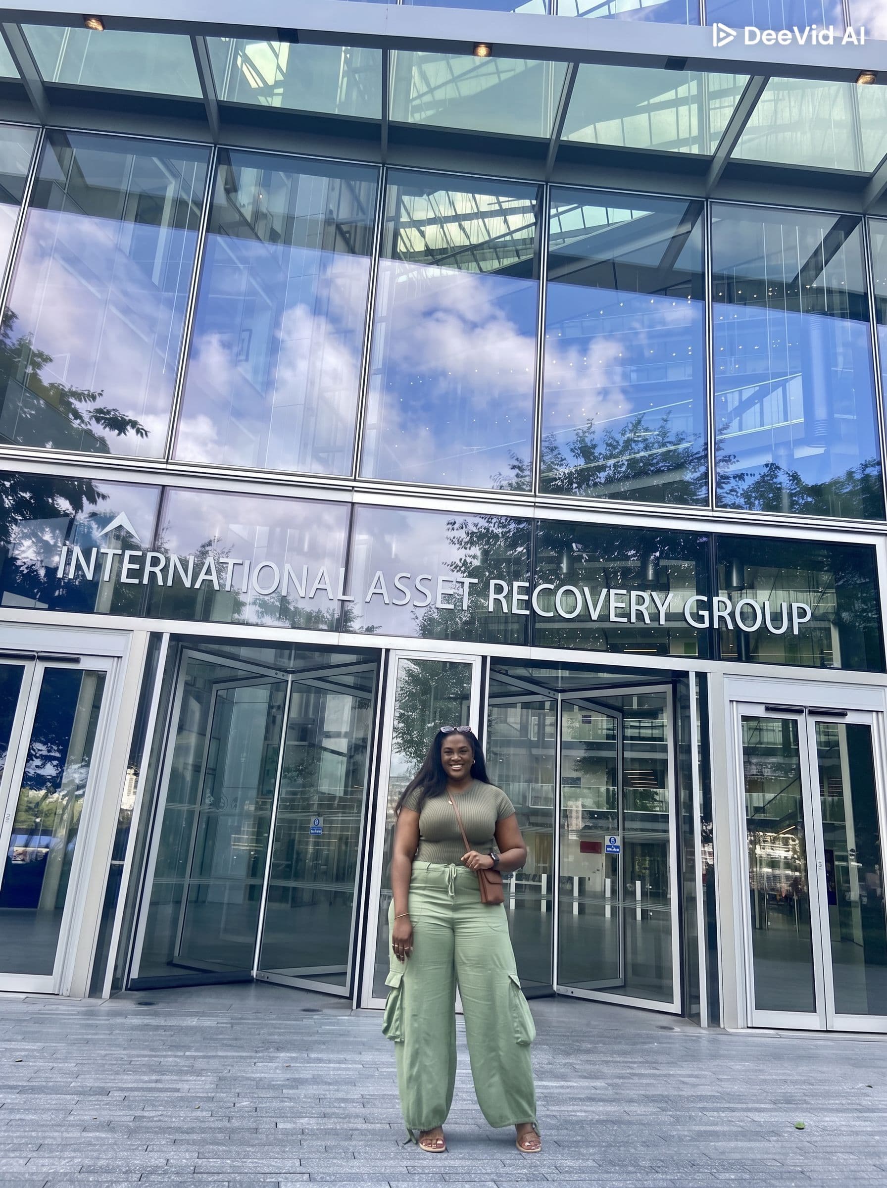 Smiling woman in green stands before the International Asset Recovery Group's modern glass building.